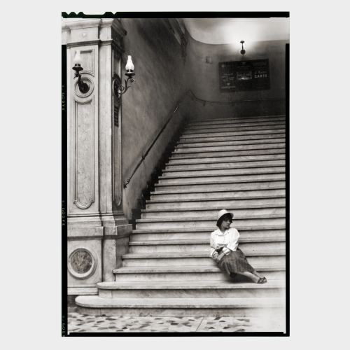 Young woman sitting at bottom of long staircase in historic building